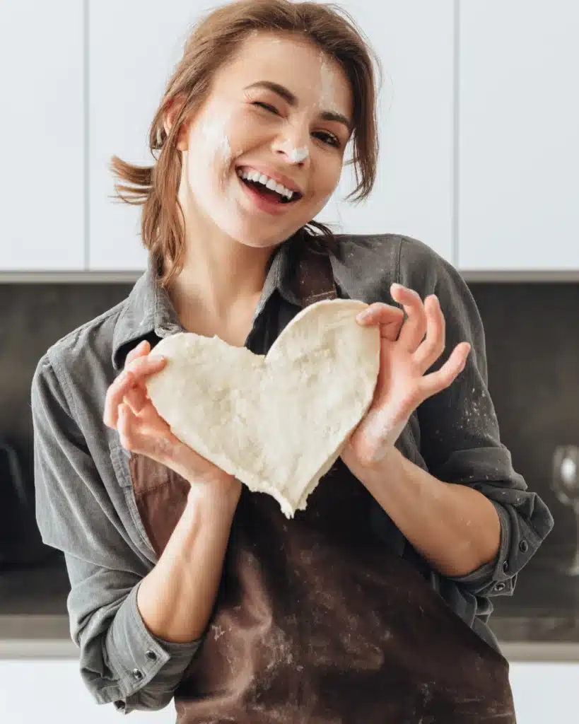 About Me 1 Healthy food blogger Clara Dellucci holding heart-shaped dough in her kitchen
